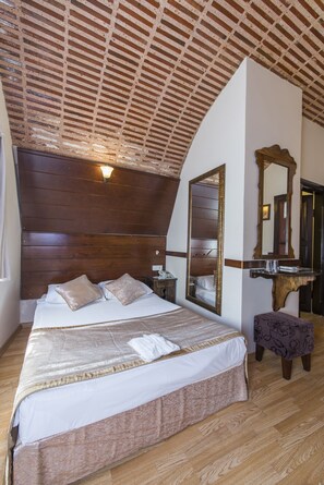 Un dormitorio con cabecera de madera, una cama grande con colcha estampada, una mesita de noche, un espejo y un banco.