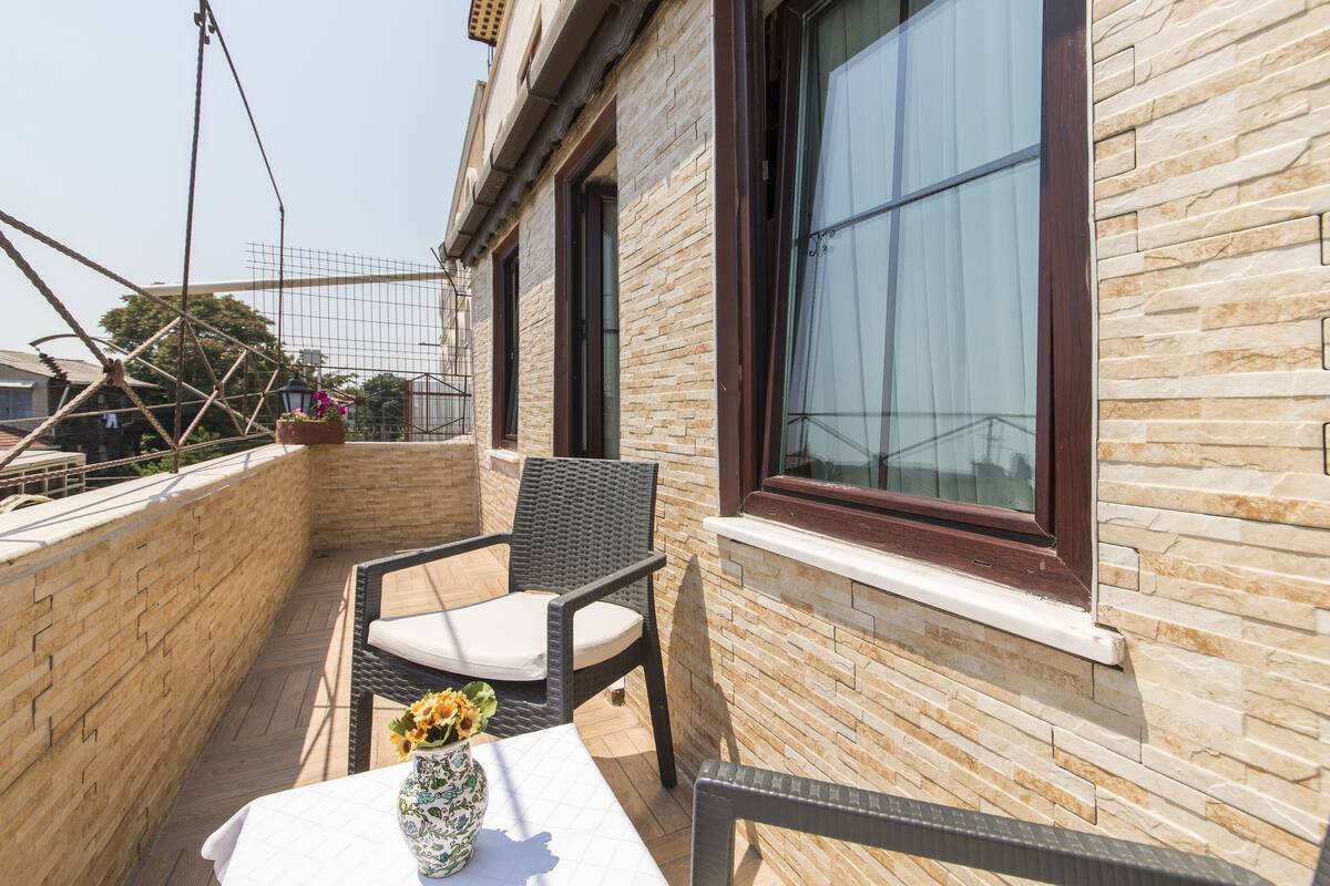 A balcony with wicker chairs, a table with a vase of flowers, and a view of the cityscape.