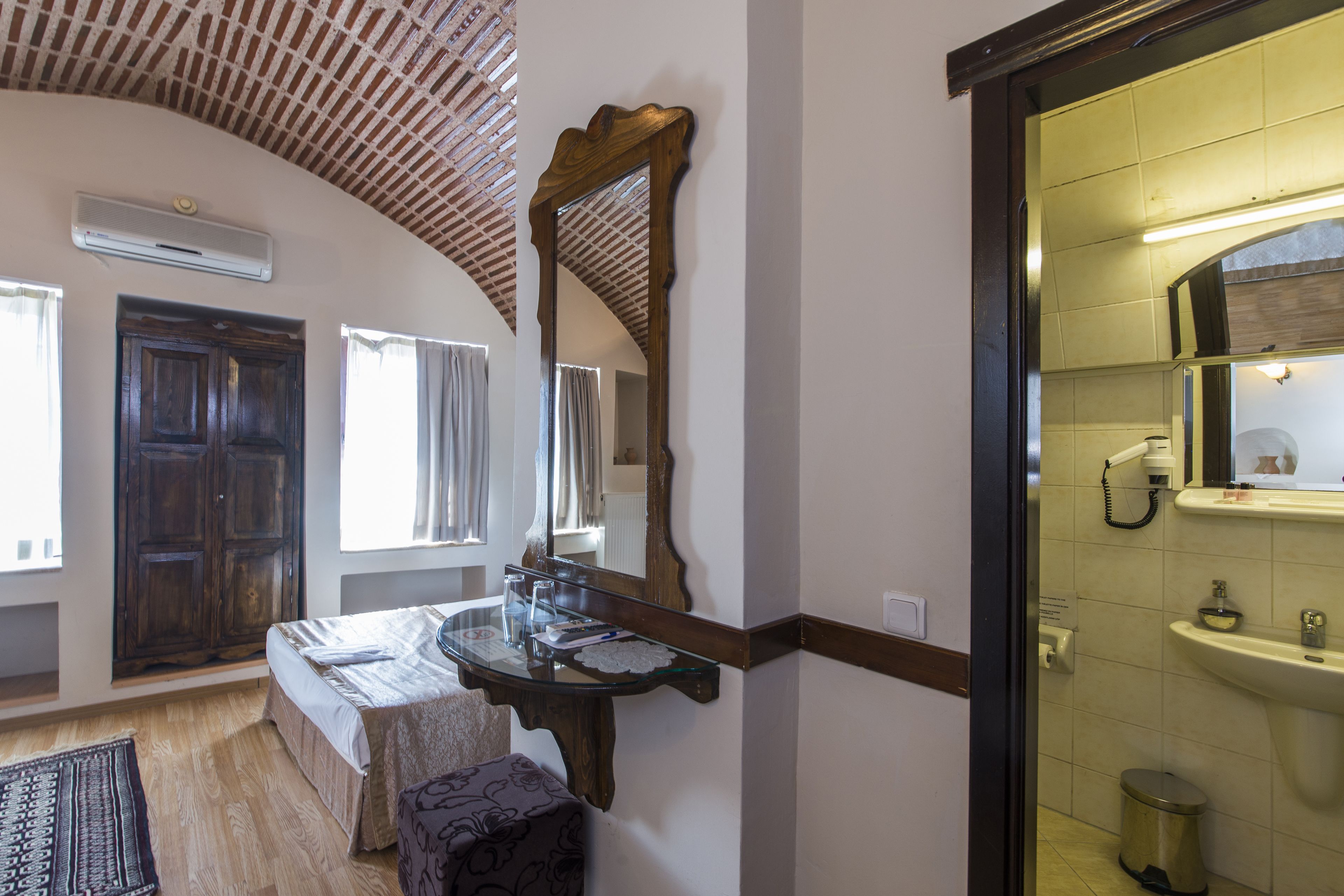 Una habitación con techo de madera, un espejo grande, una cama, una mesita de noche y un baño con lavabo e inodoro.