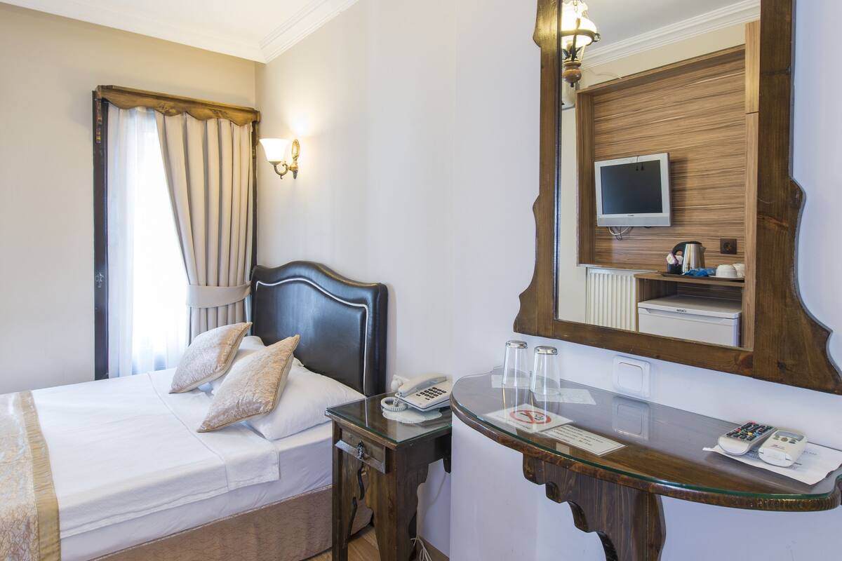 A hotel room with a bed, bedside table, mirror, and a small stool.