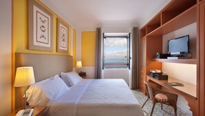 A hotel room with a bed, bedside table with a lamp, a desk with a chair, a television, and framed artwork on the wall. - Hotel Minerva (Sorrento)
