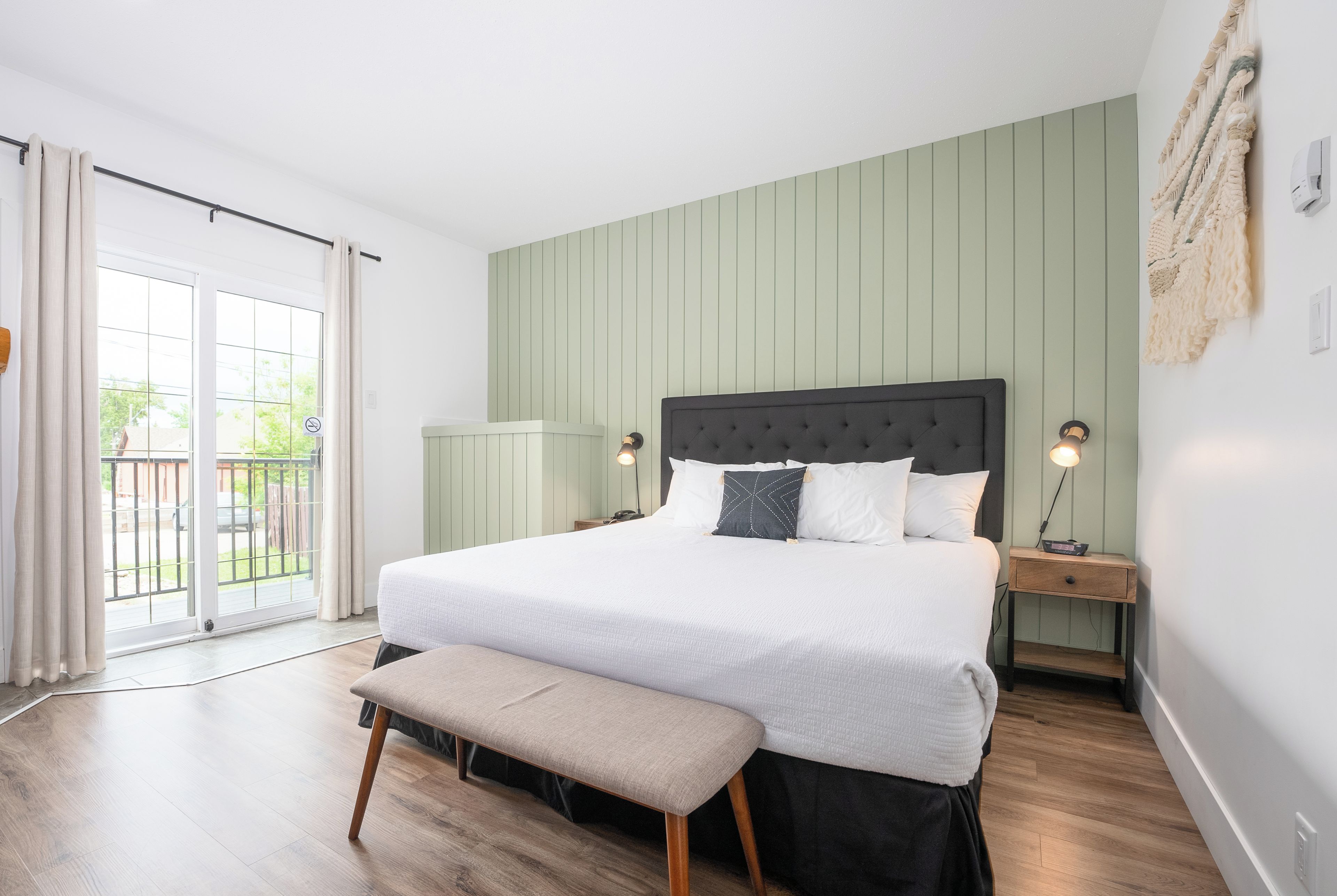 A bedroom with a bed, bench, bedside tables, and a view through a sliding door.