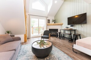 Ein modernes Wohnzimmer mit einer Couch, einem Couchtisch mit Pflanze, einem Kamin und einem an der Wand montierten Fernseher.