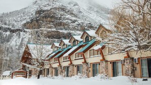 Een rij chalets met stenen muren en houten daken, met een besneeuwde berg op de achtergrond.