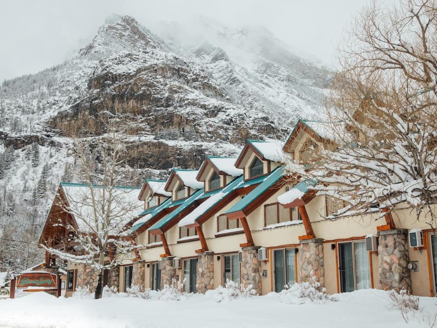 Une rangée de bâtiments de style chalet, avec des murs en pierre et des toits en bois, se dressant sur fond de montagnes enneigées.