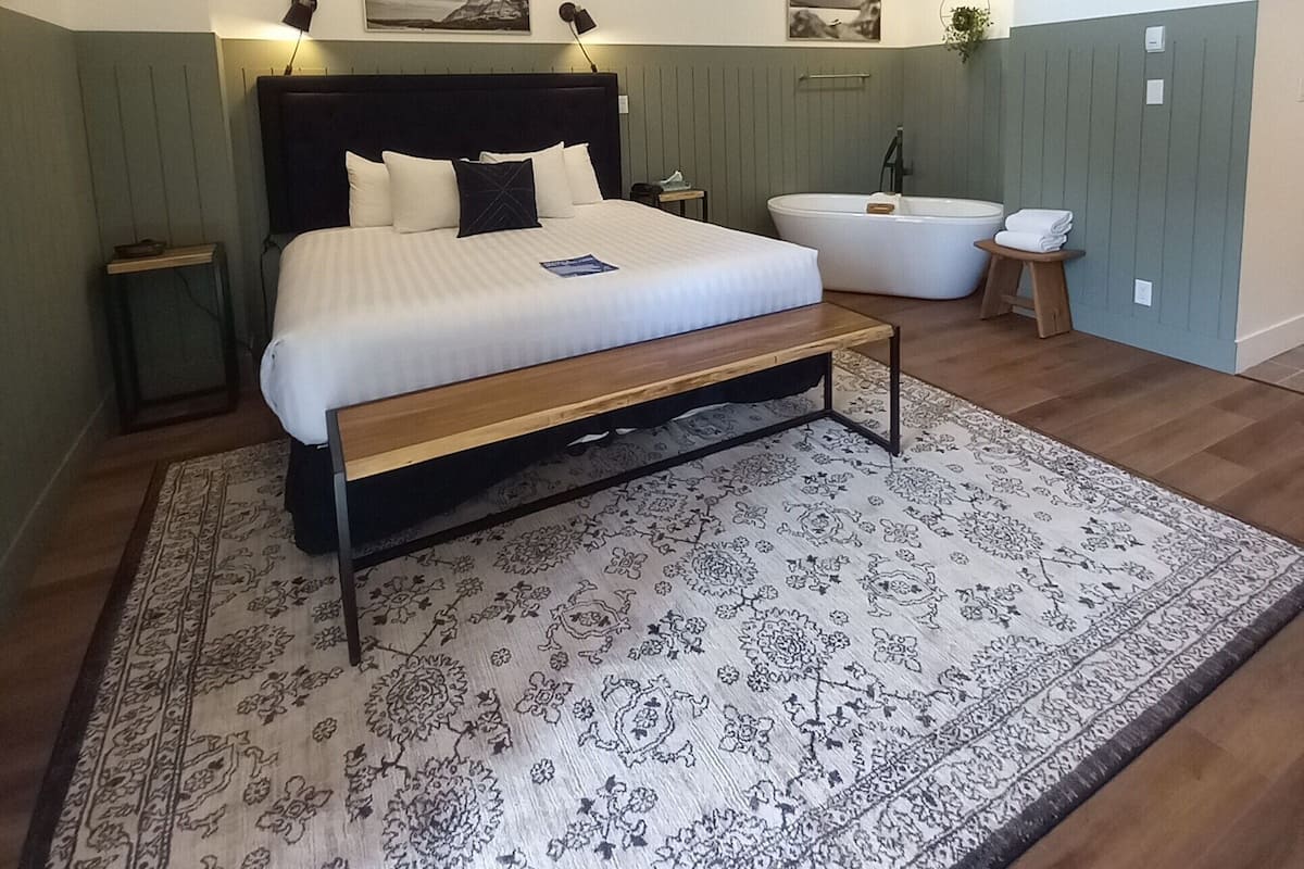 Une chambre à coucher avec un grand lit, un banc en bois, un tapis à motifs, une baignoire et un lustre.