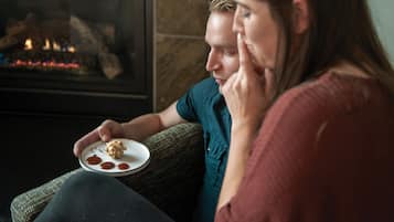A person holding a plate with food, sitting on a couch in a room with a fireplace.