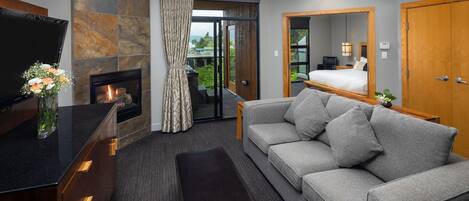 A modern hotel room with a fireplace, a sofa, a TV, and a large mirror.