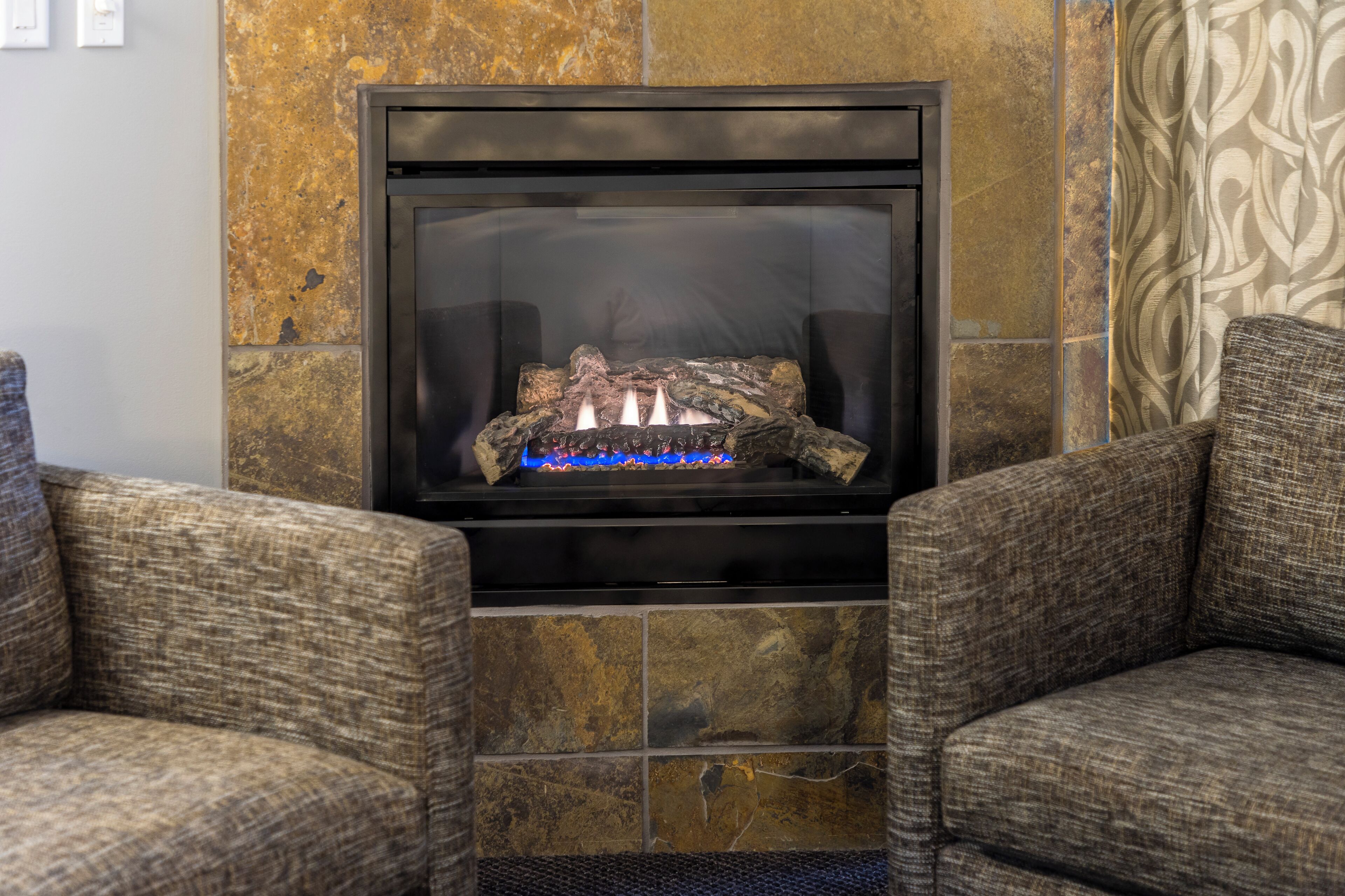 A fireplace with a log fire, flanked by two upholstered armchairs.