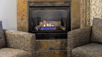 A fireplace with a log fire, flanked by two upholstered armchairs.