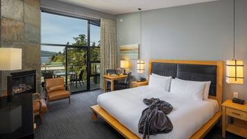 A hotel room with a large bed, a desk, a chair, a fireplace, and a view of the outdoors.