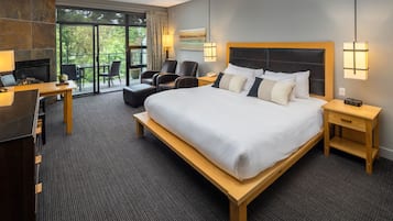 A hotel room with a large bed, a desk, a chair, a TV, and a fireplace.