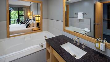 Une salle de bain moderne dotée d’un grand miroir, d’une baignoire, d’un lavabo et offrant une vue sur une chambre à coucher avec un lit et un balcon.