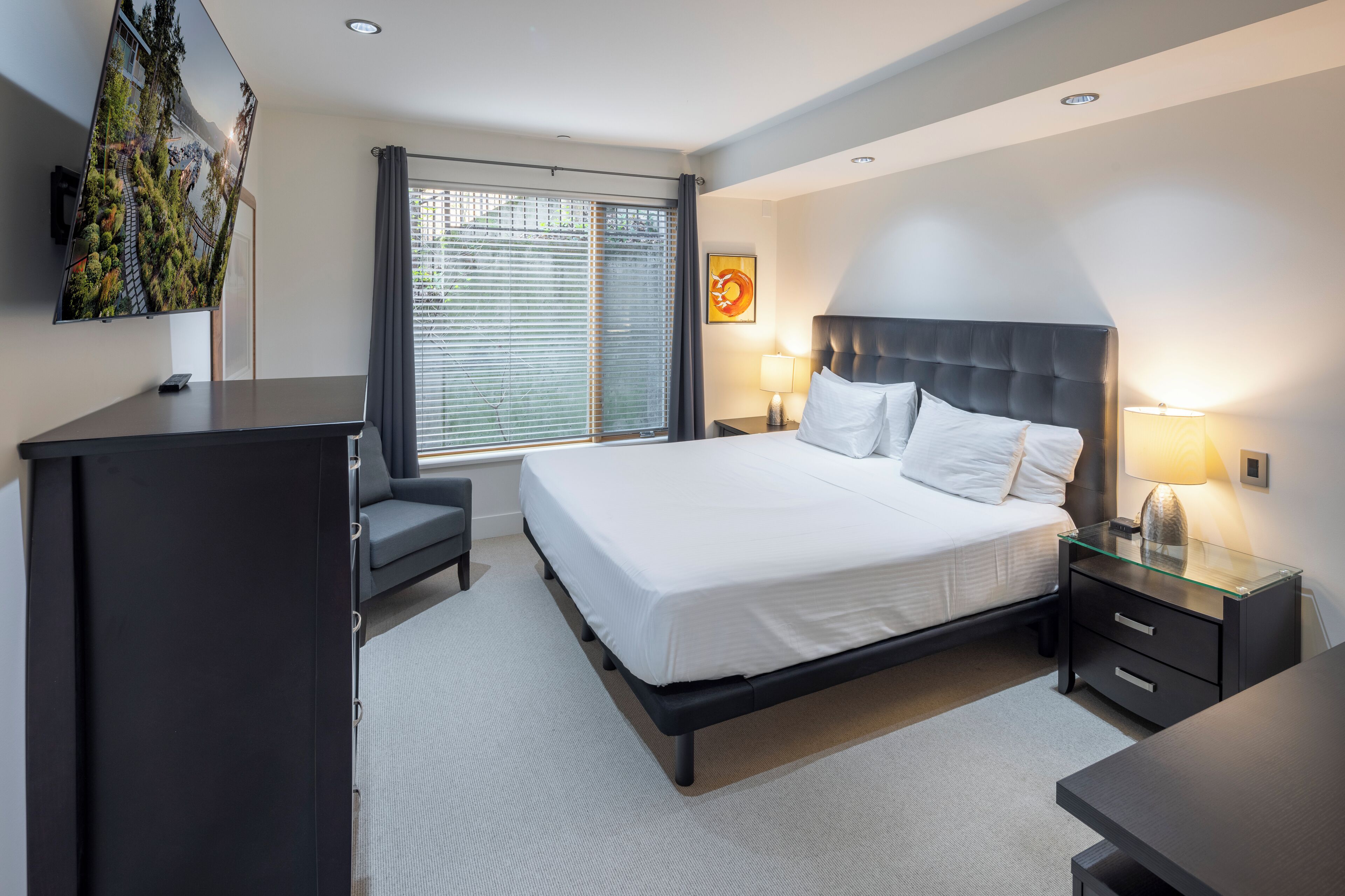 A modern hotel room with a large bed, bedside tables, a desk, and a TV.