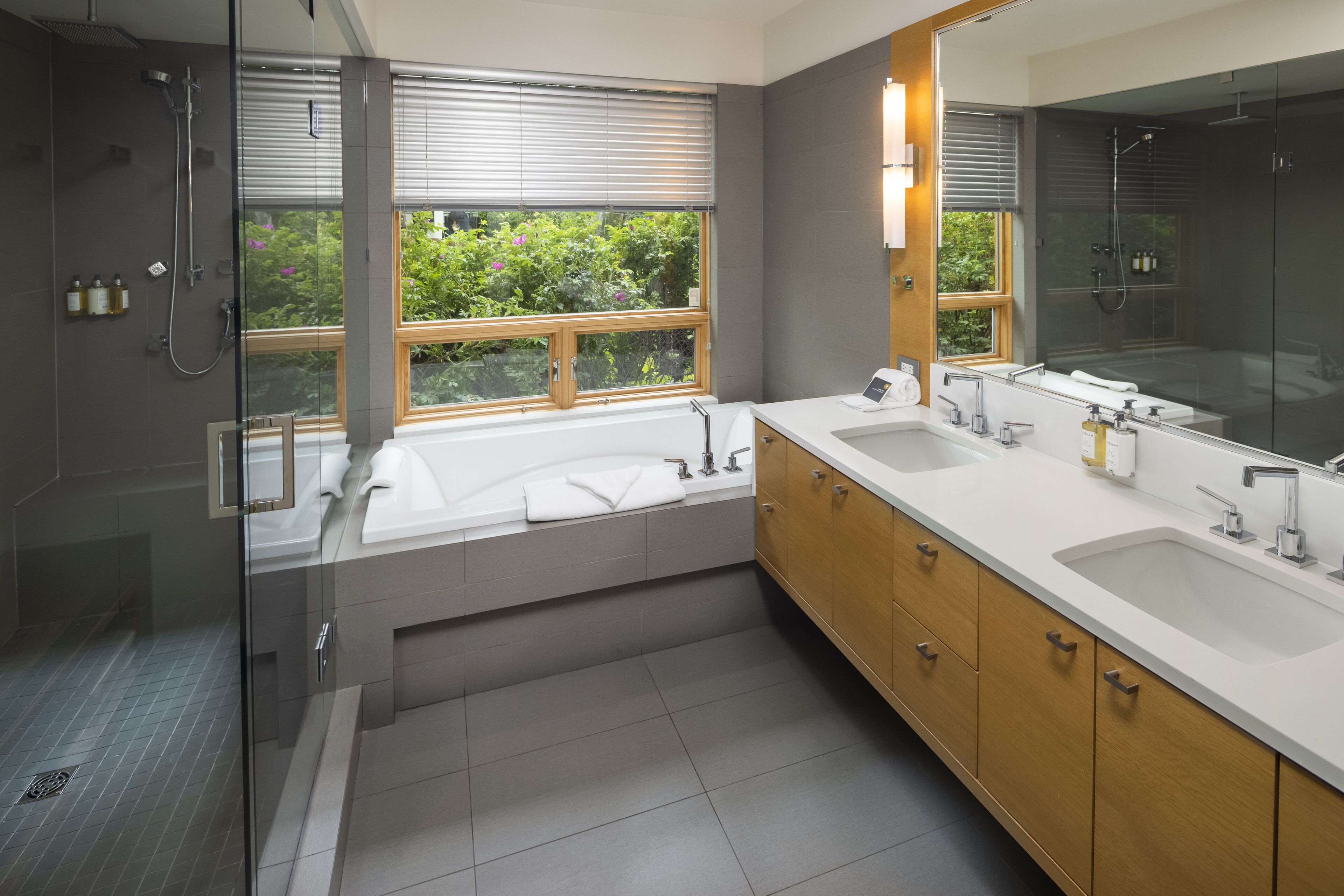 A modern bathroom with dual sinks, a large mirror, and a glass-enclosed shower.