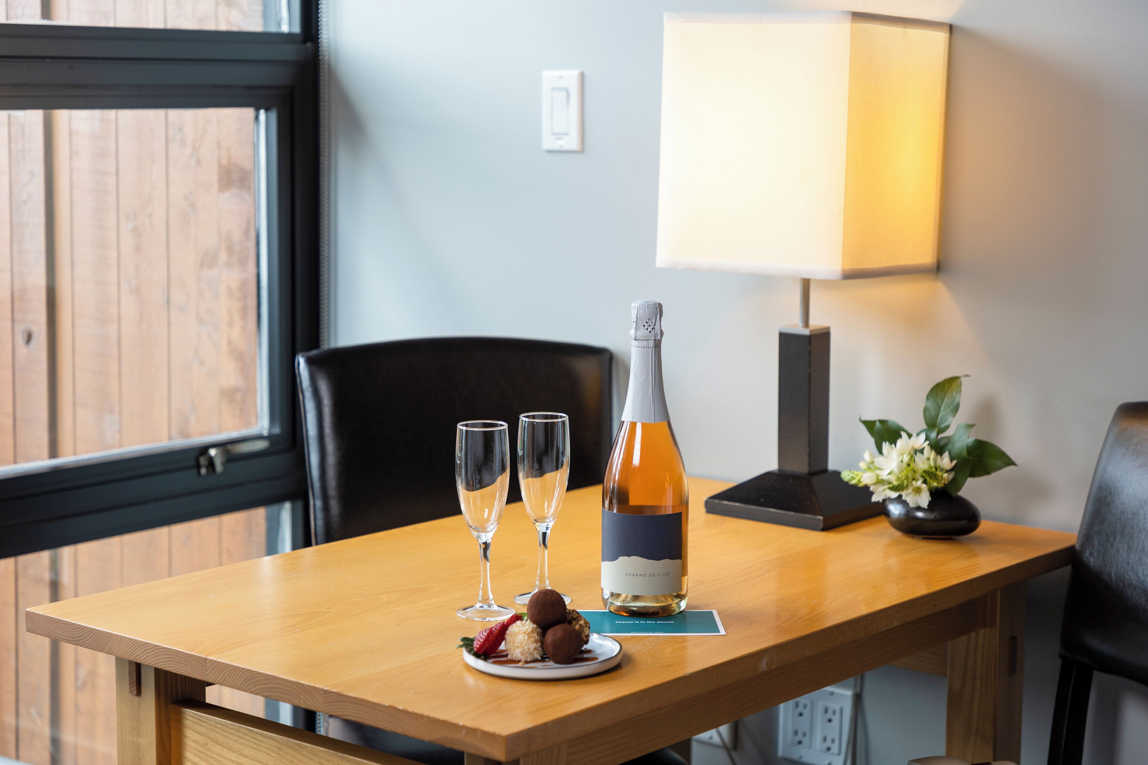 A wooden table with a bottle of wine, two glasses, and a plate with food.
