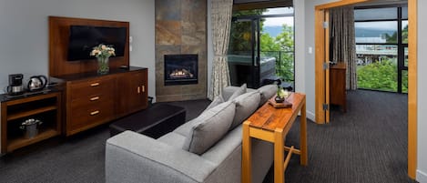 A modern living room with a grey sofa, a flat-screen TV, a fireplace, and a balcony with a view of the sea.