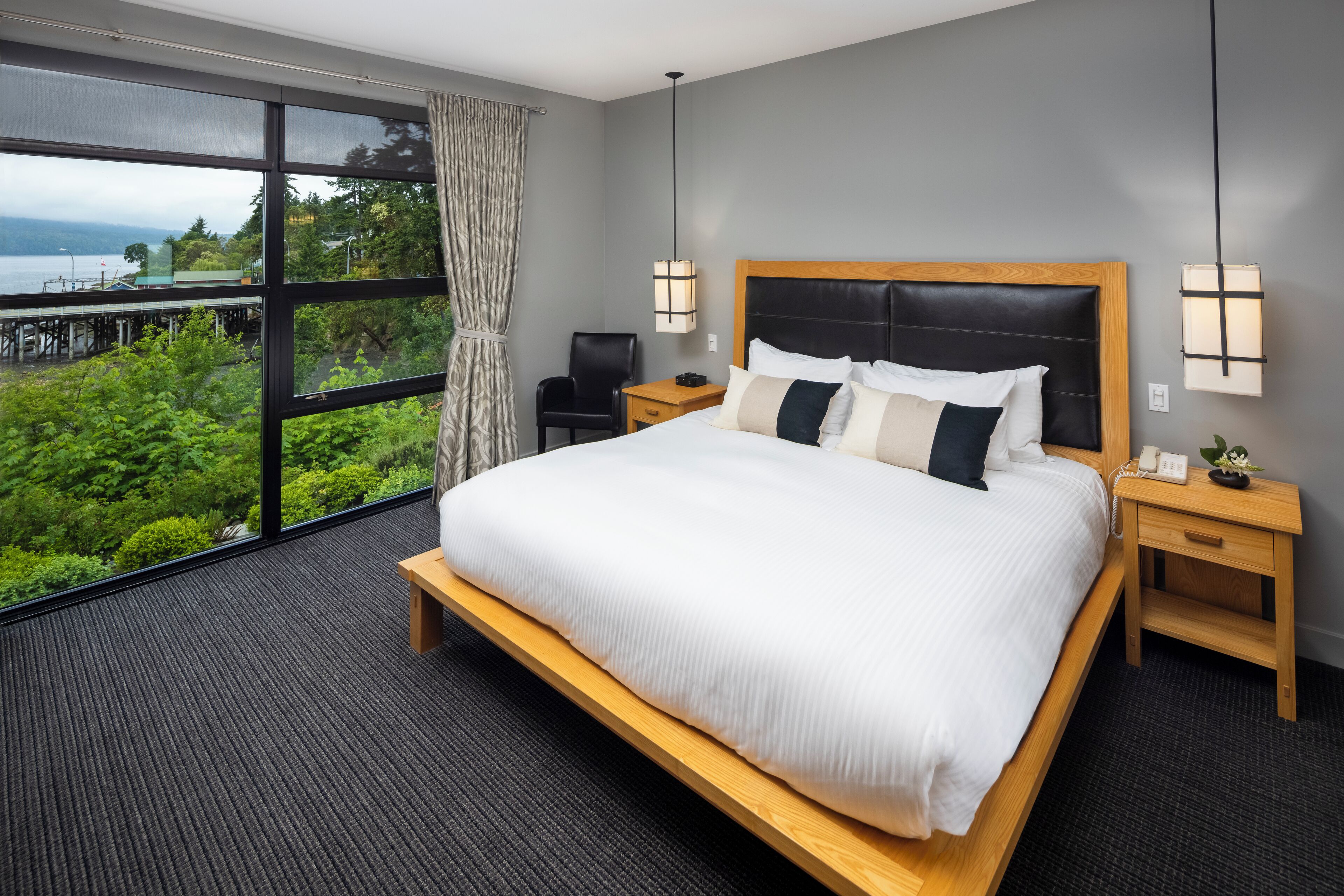 Ein Hotelzimmer mit einem großen Bett, einem Schreibtisch, einem Stuhl und Blick auf Grünflächen und Wasser.