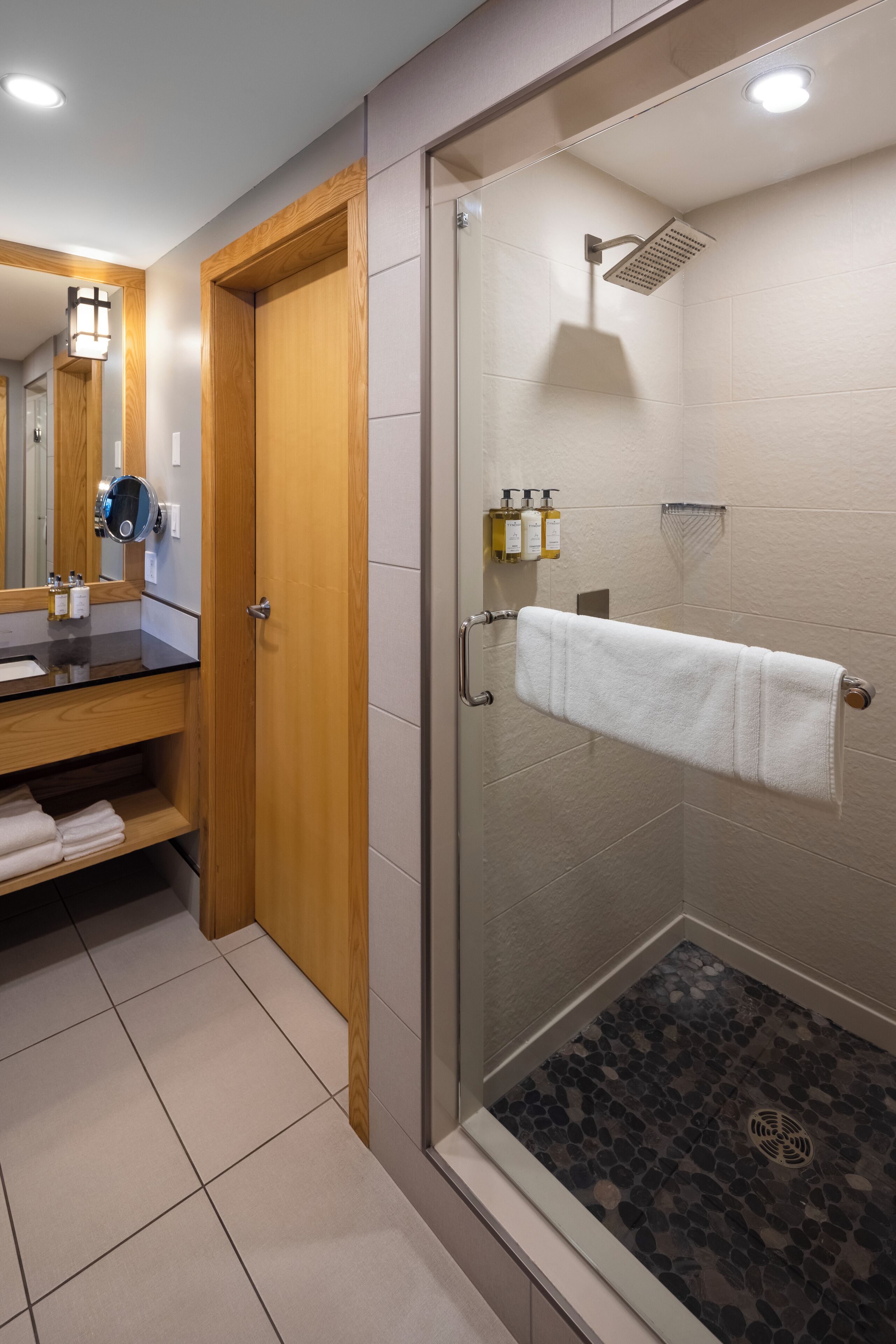 A modern bathroom with a glass-enclosed shower, a wooden vanity with a mirror, and a towel rack.