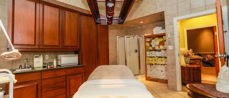 A spa room with a massage table, wooden cabinets, a shower area, and a towel rack.