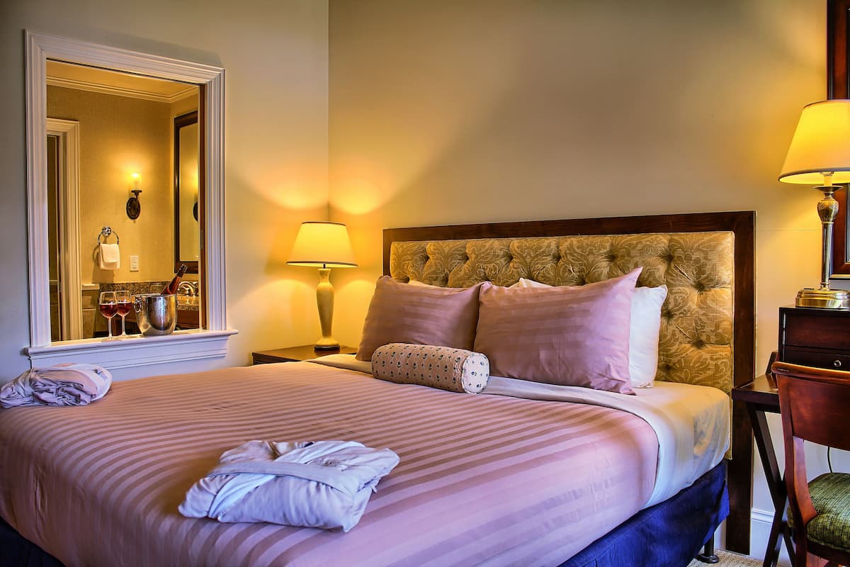A neatly made bed with striped bedding, a headboard with a floral pattern, and a bedside table with a lamp.