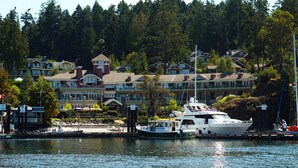 A waterfront property with multiple buildings, a dock with boats, and a forested hillside in the background. - Poets Cove Resort & Spa (Pender Island)