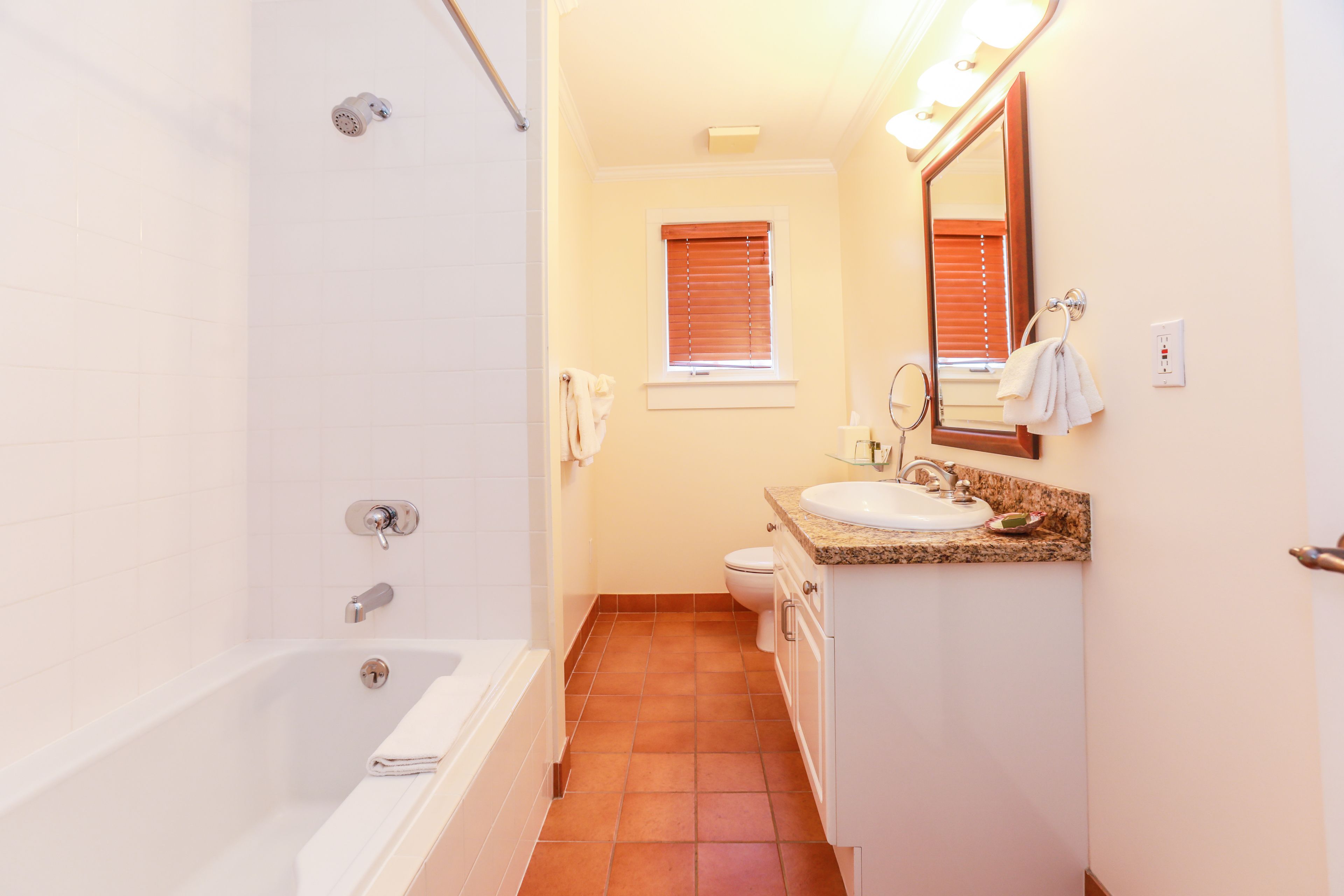 A bathroom with a bathtub, toilet, sink, and a window with blinds.
