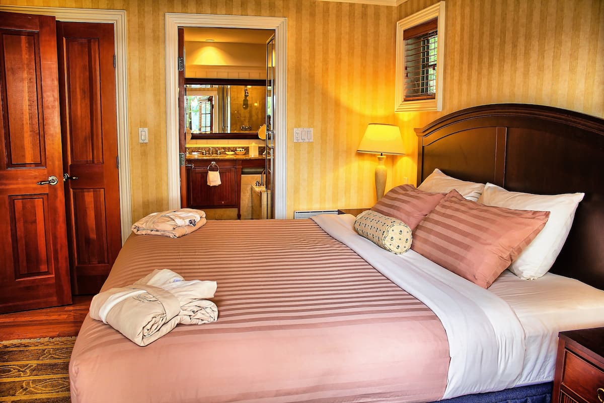 A hotel room with a large bed, a wooden headboard, and a bathroom visible through an open door.