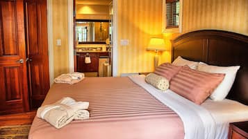 Una habitación de hotel con una cama grande, un cabecero de madera y un baño visible a través de una puerta abierta.