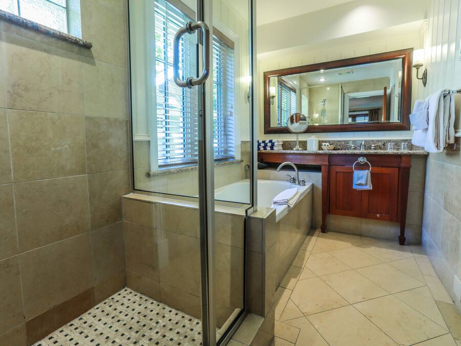 Un baño moderno con cabina de ducha de vidrio, bañera, lavabo con tocador y un espejo grande sobre el lavabo.