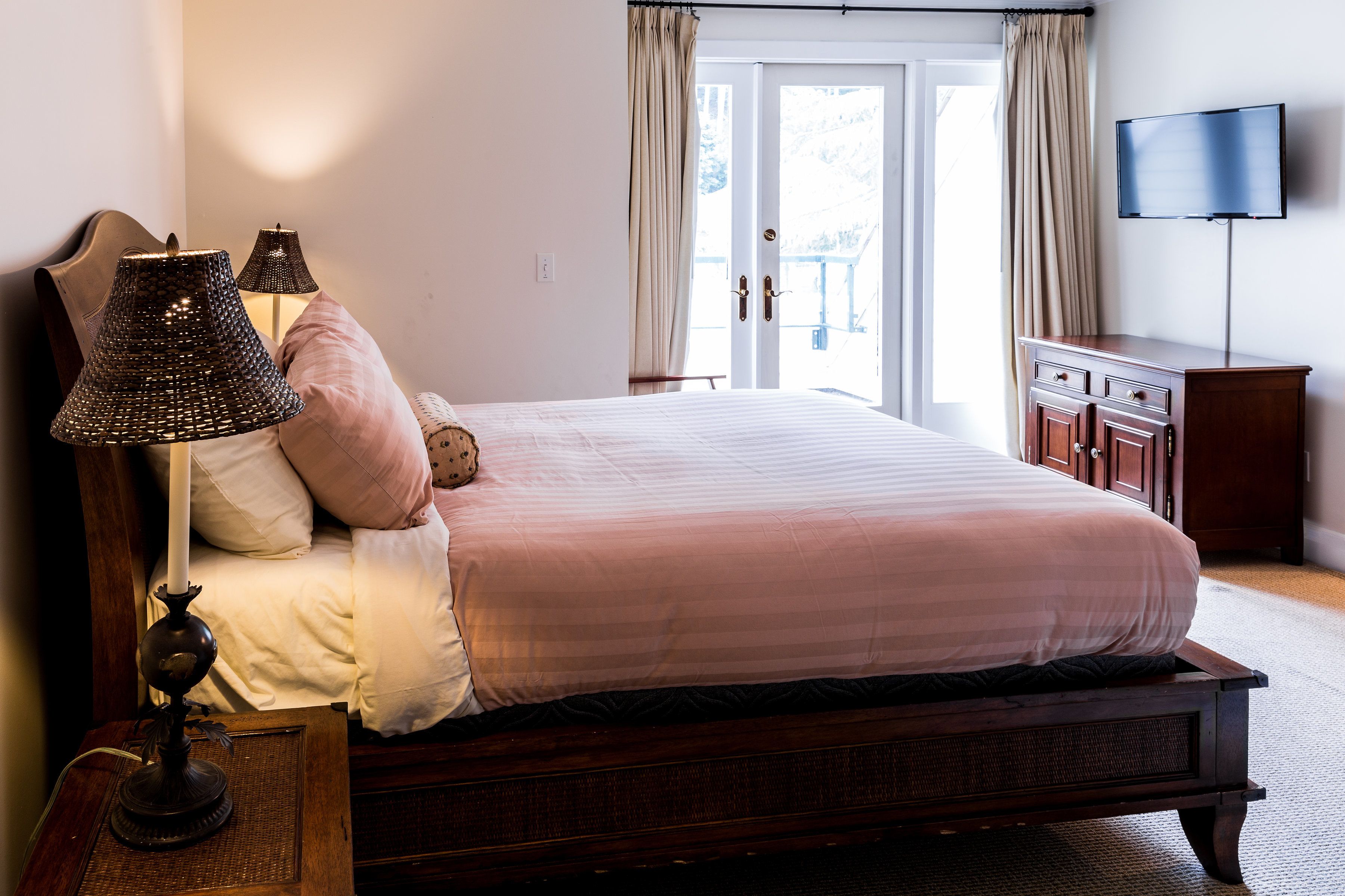 Une chambre avec un grand lit, deux lampes de chevet, une table de chevet en bois, une commode et un téléviseur fixé au mur.