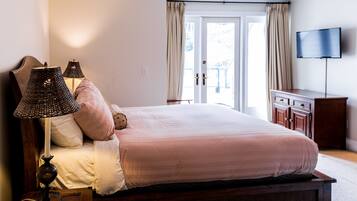 A bedroom with a large bed, two bedside lamps, a wooden nightstand, a dresser, and a television on the wall.