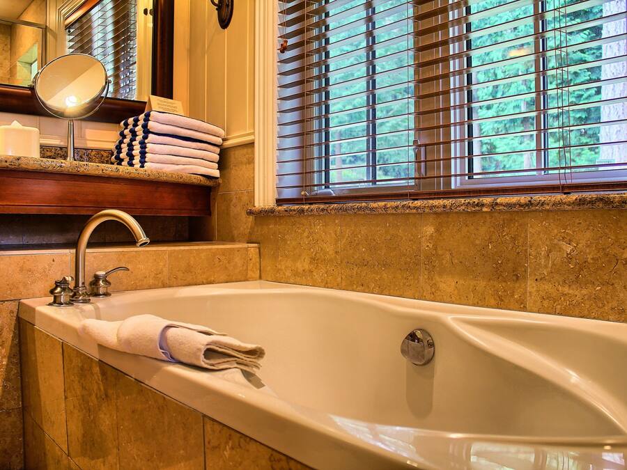 A bathroom with a large bathtub, a mirror, a towel rack, and a window with blinds.
