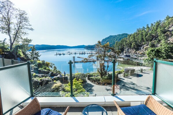Un balcón con vistas a un lago, barcos amarrados y una ladera boscosa.