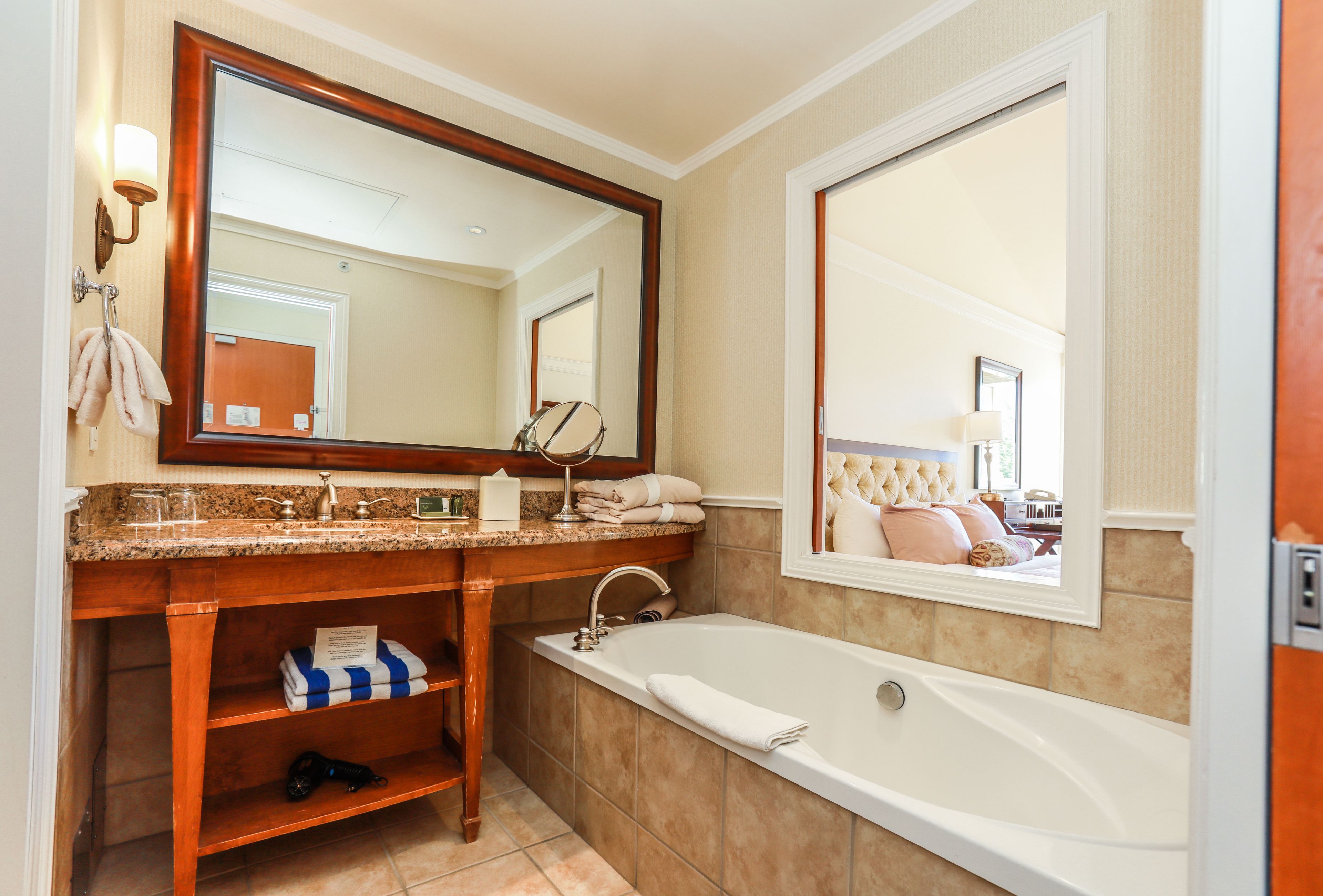 A bathroom with a large mirror, a bathtub, a vanity with a sink, and a towel rack.