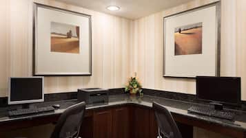 A hotel office with two desks, each with a computer and keyboard, framed artwork on the walls, and a small plant on the counter.