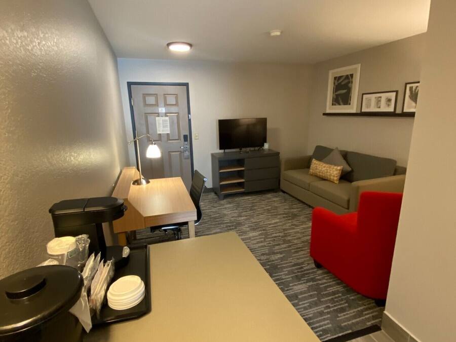 Una sala compacta con un sofá, un sillón rojo, un televisor y una zona para café.