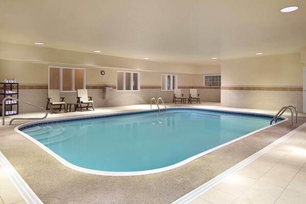A large indoor swimming pool with a tiled edge, surrounded by lounge chairs and a small table.