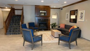 A living room with a fireplace, a staircase, and a sofa. - Country Inn & Suites by Radisson, Champaign North, IL (Champaign)