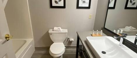 Un baño con bañera, inodoro y lavamanos. Hay cuadros enmarcados en la pared.