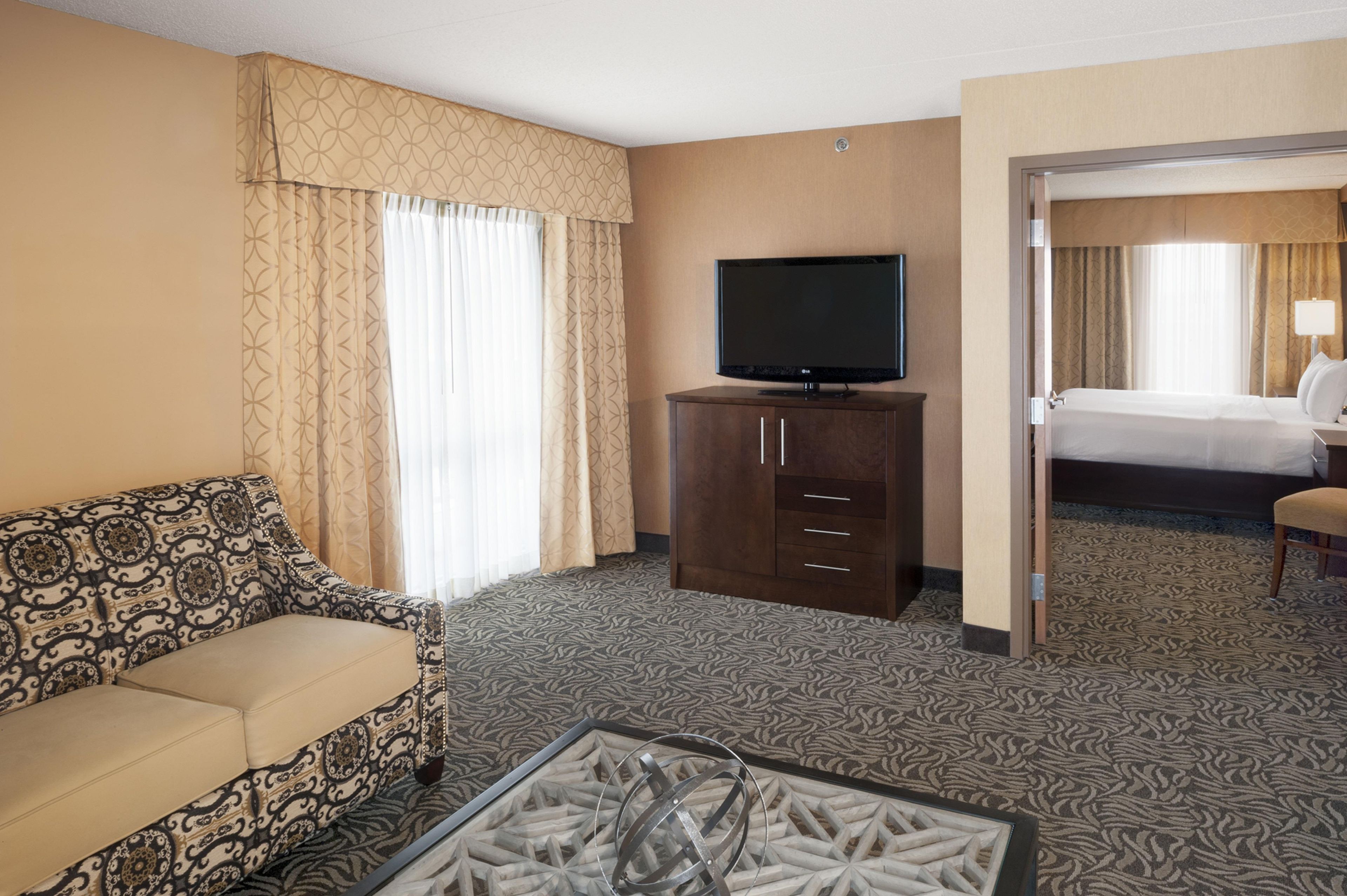 A hotel room with a sofa, a television on a cabinet, a bed, and a patterned carpet.