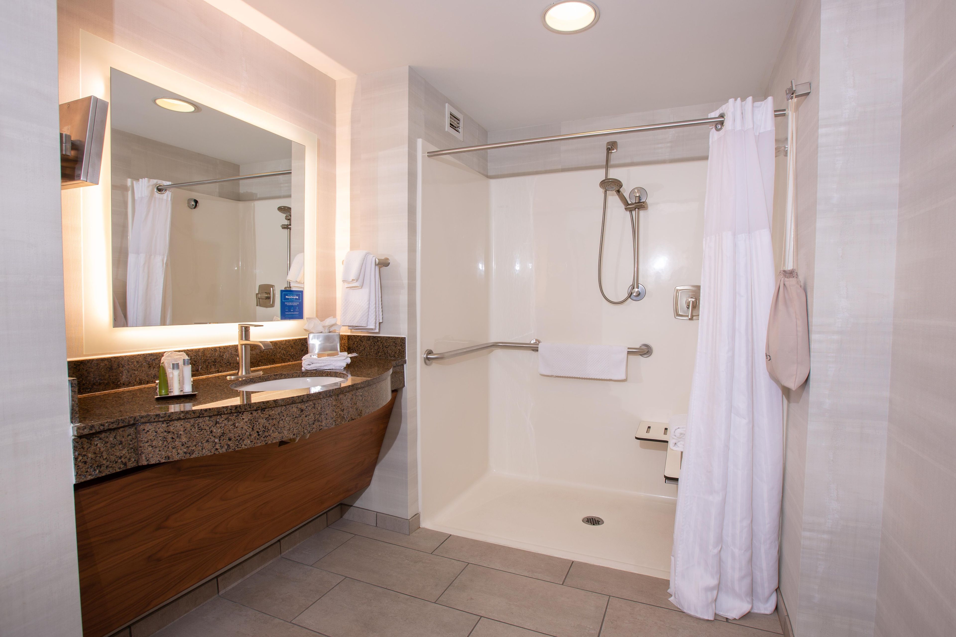 A modern bathroom with a granite countertop sink, a mirror, a shower with a glass door, and a towel rack.