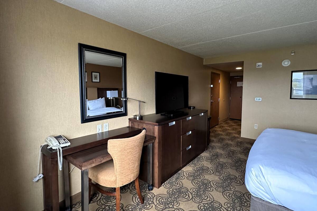 Une chambre d’hôtel comprenant un lit, un bureau avec un téléphone, une chaise, une télévision et un miroir.