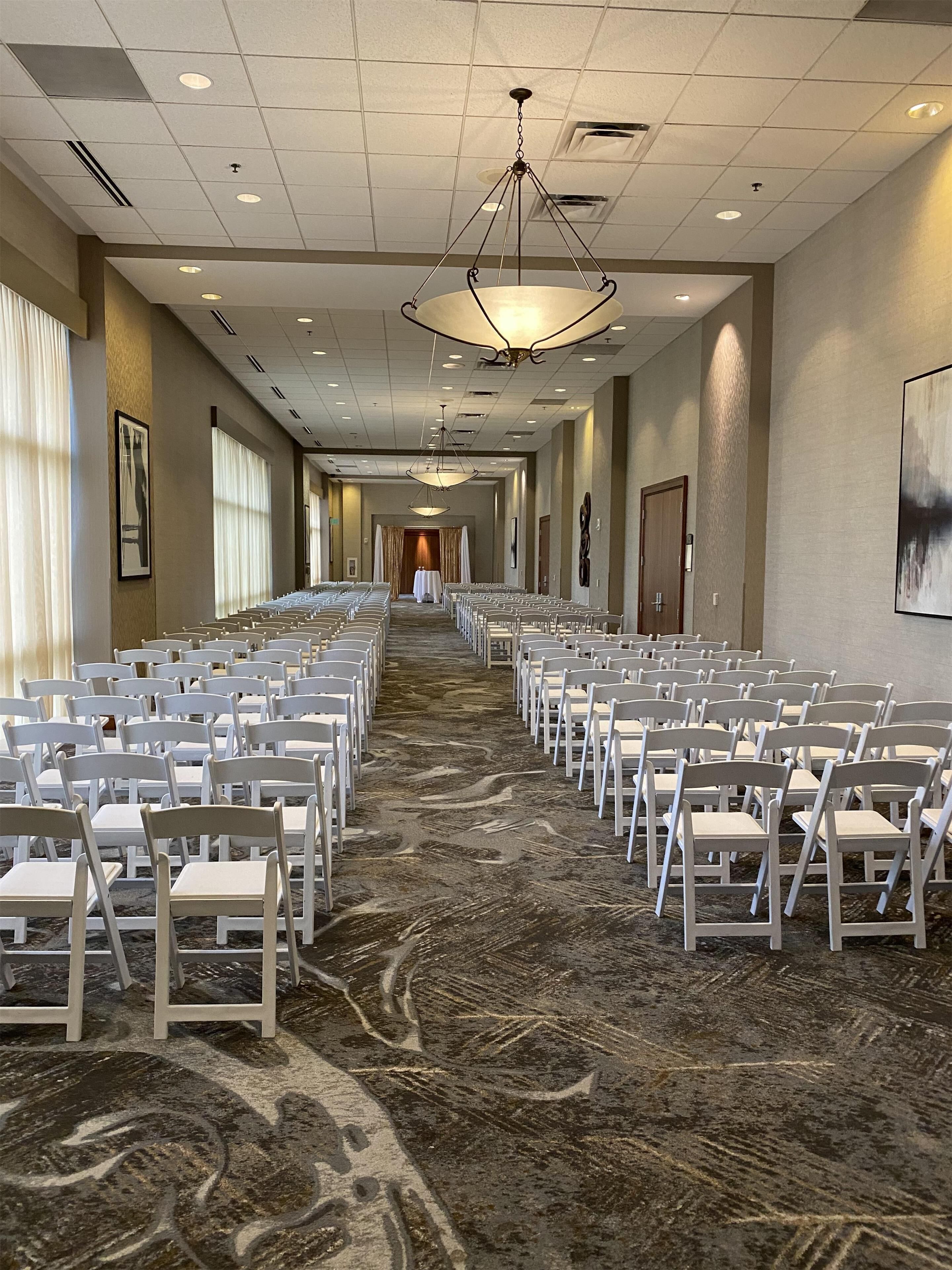 A hotel conference room with rows of white chairs, a patterned carpet, and a chandelier.