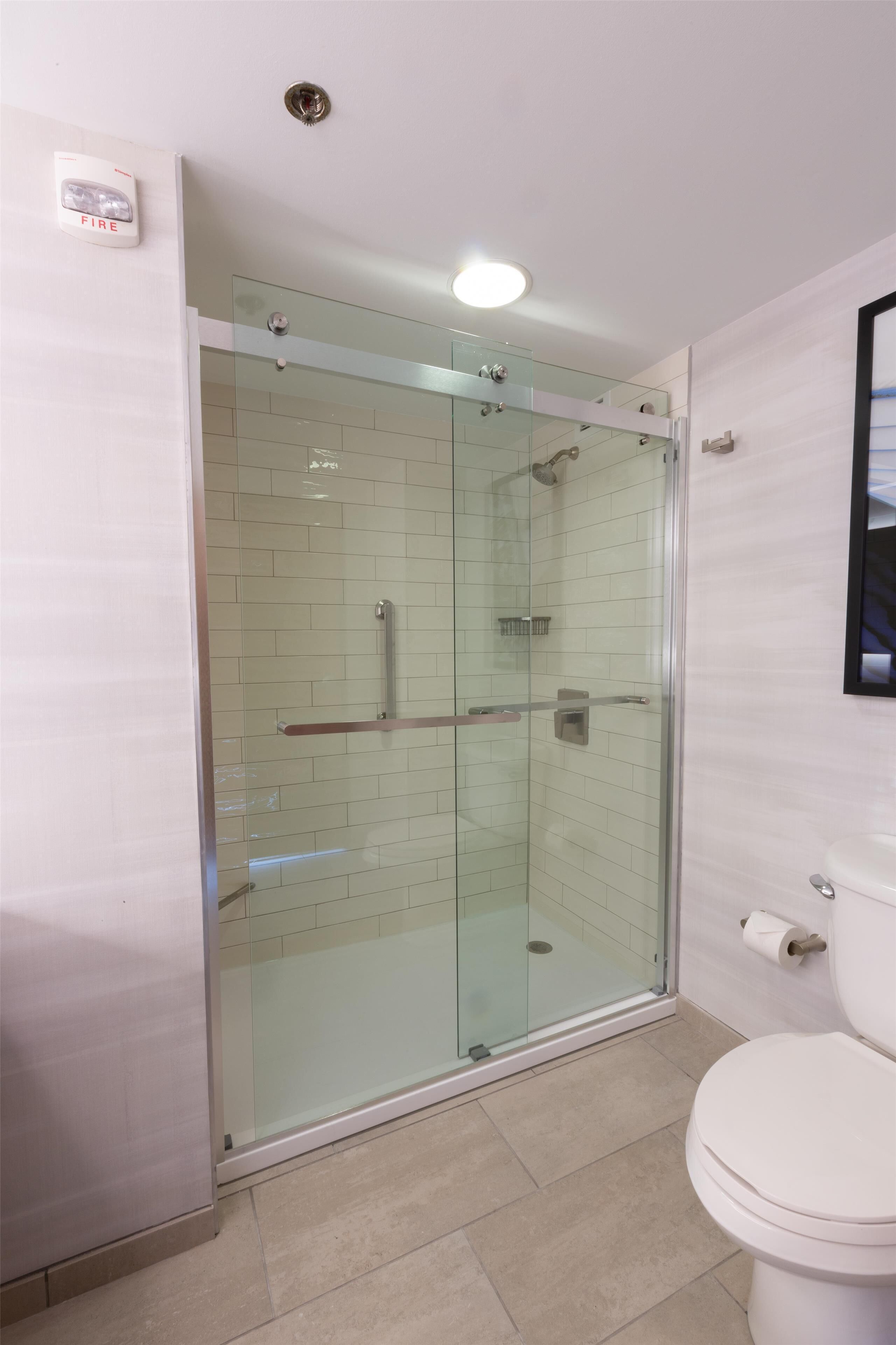 Une salle de bain moderne avec une douche en verre, des toilettes et un détecteur d’incendie bien visible.
