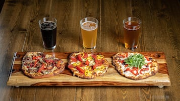 Three pizzas on a wooden board with three glasses of beer.