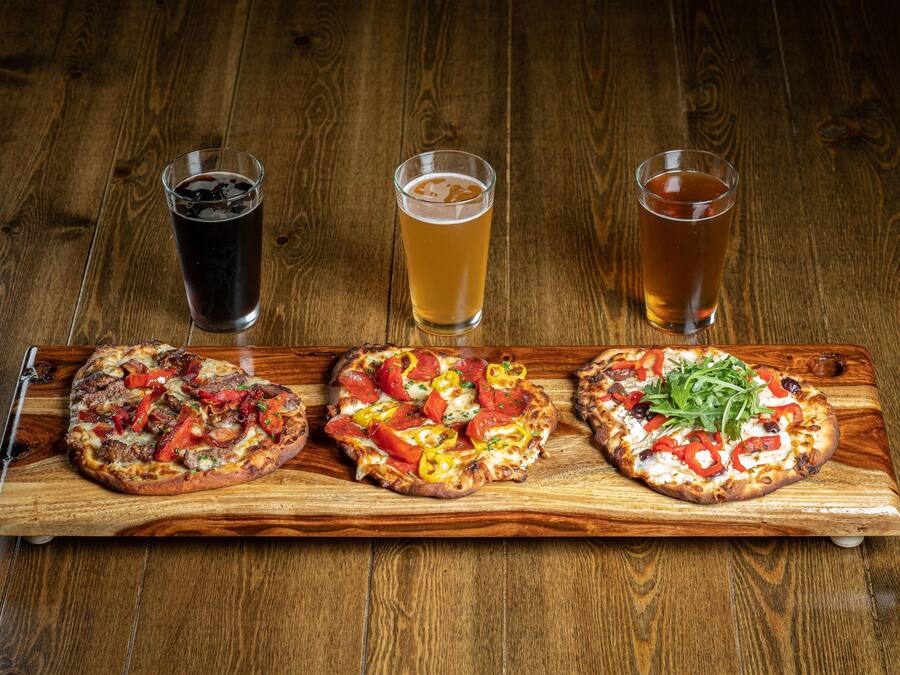 Three pizzas on a wooden board with three glasses of beer.