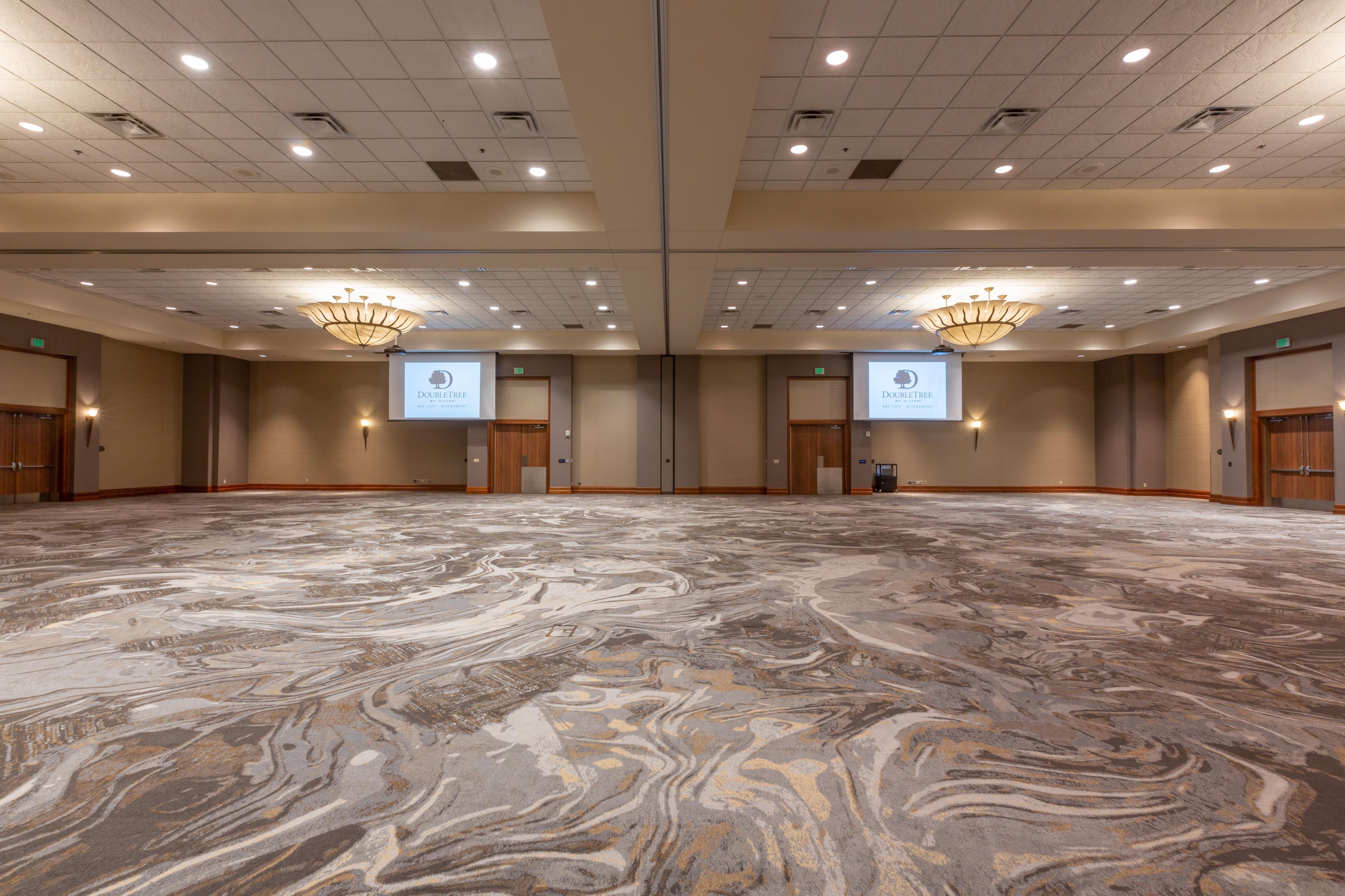A large conference room with a marble floor, multiple doors, and two large screens displaying a logo.