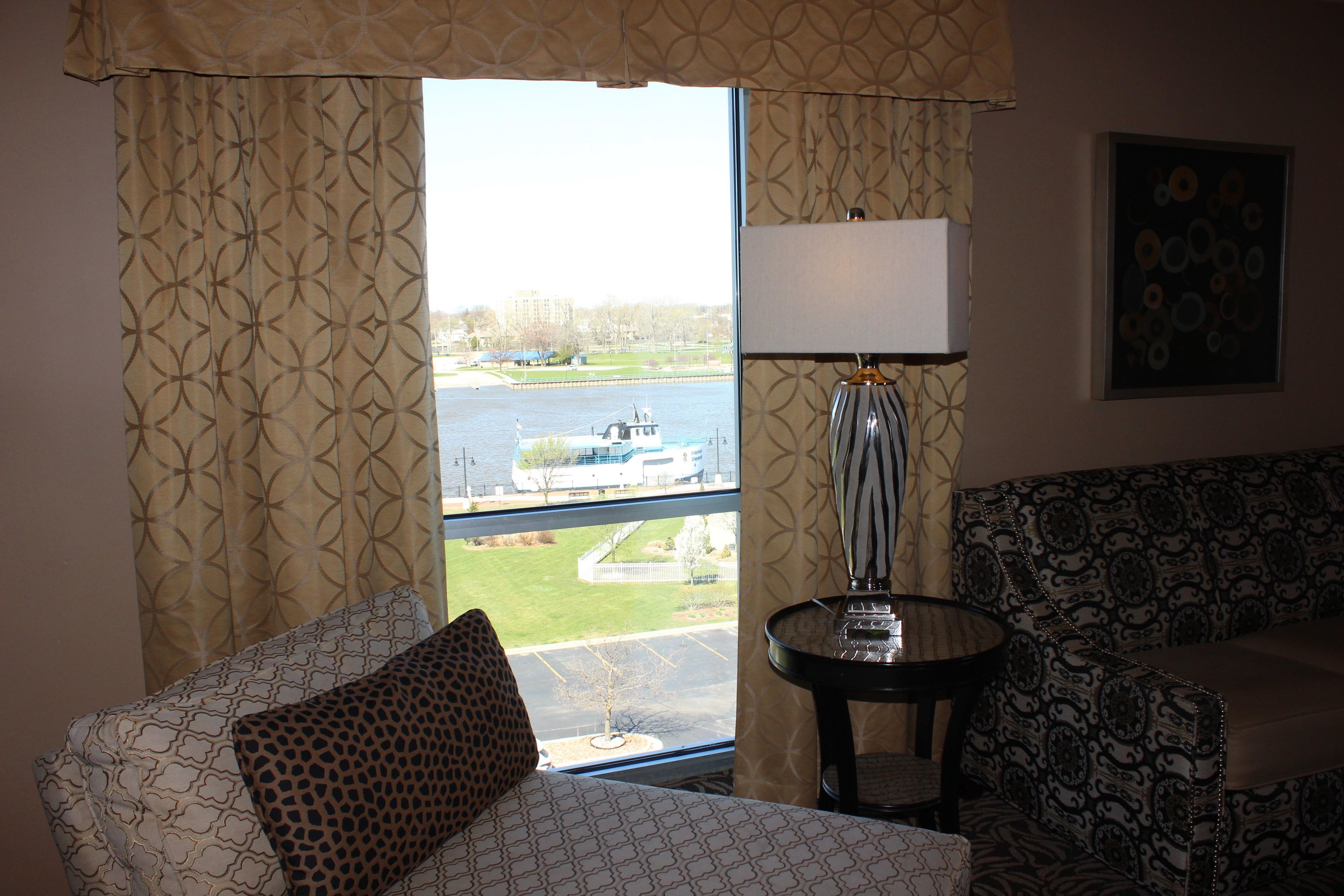 A room with a view of a body of water, a lamp, and patterned furniture.