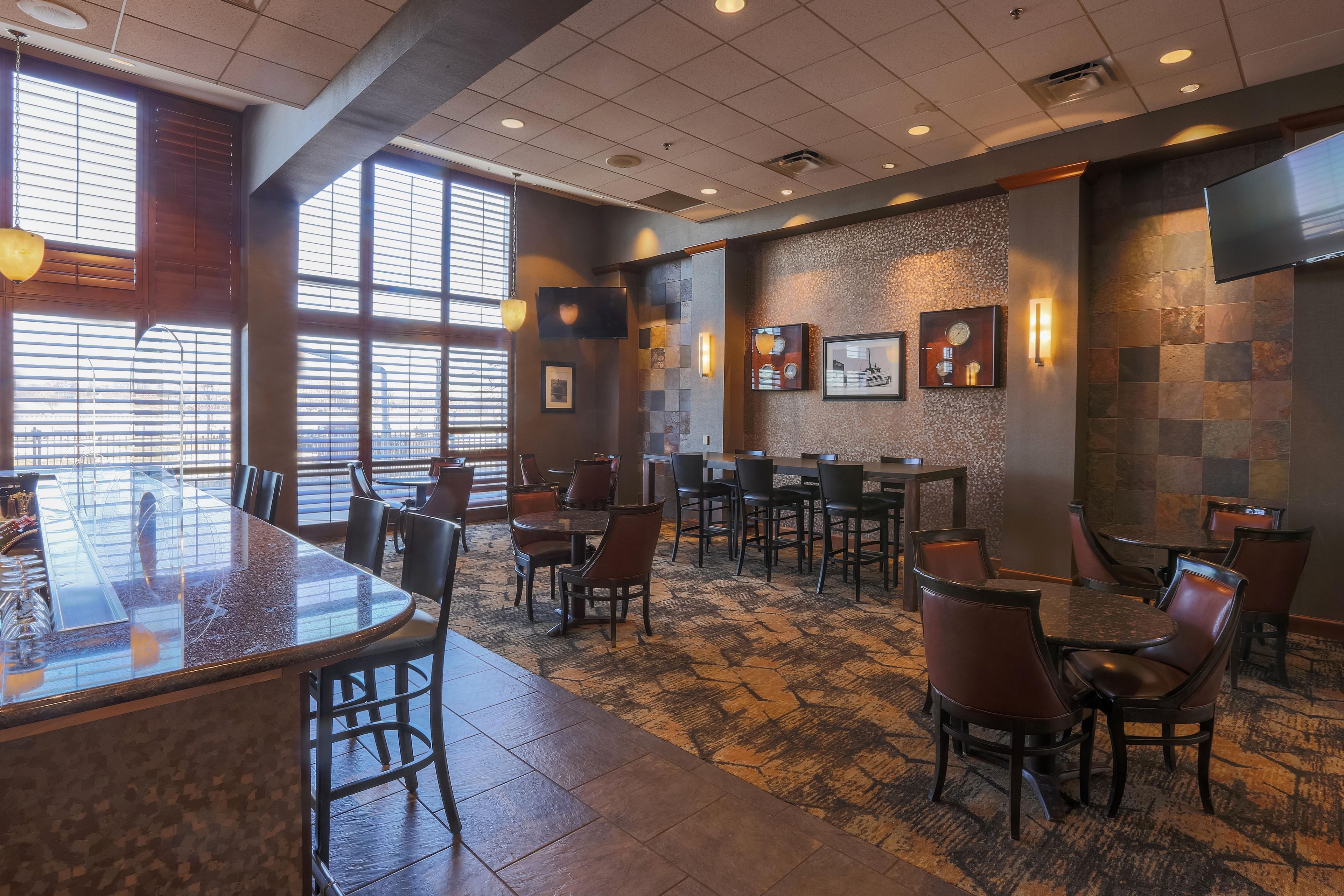 A hotel lobby with a bar area, seating arrangements, and a large window providing natural light.